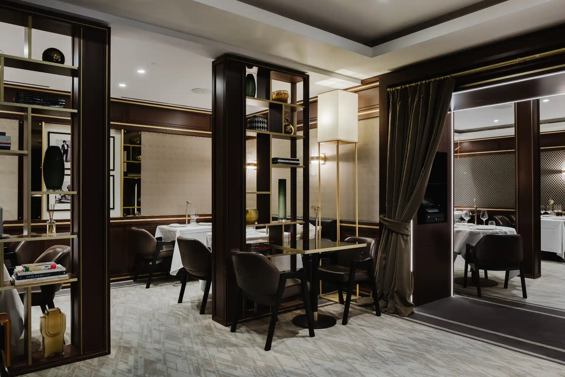 Luxury fine dining restaurant interior with dark wood shelving dividers, elegant lighting, and set dining tables.