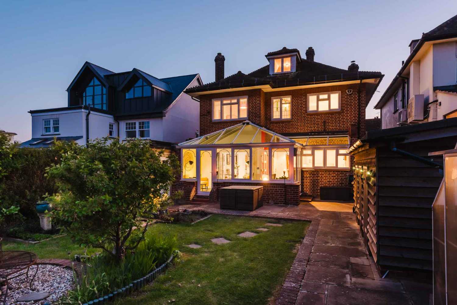 Exterior architectural photography of a brick house at dusk featuring a glowing conservatory and landscaped garden in Essex.