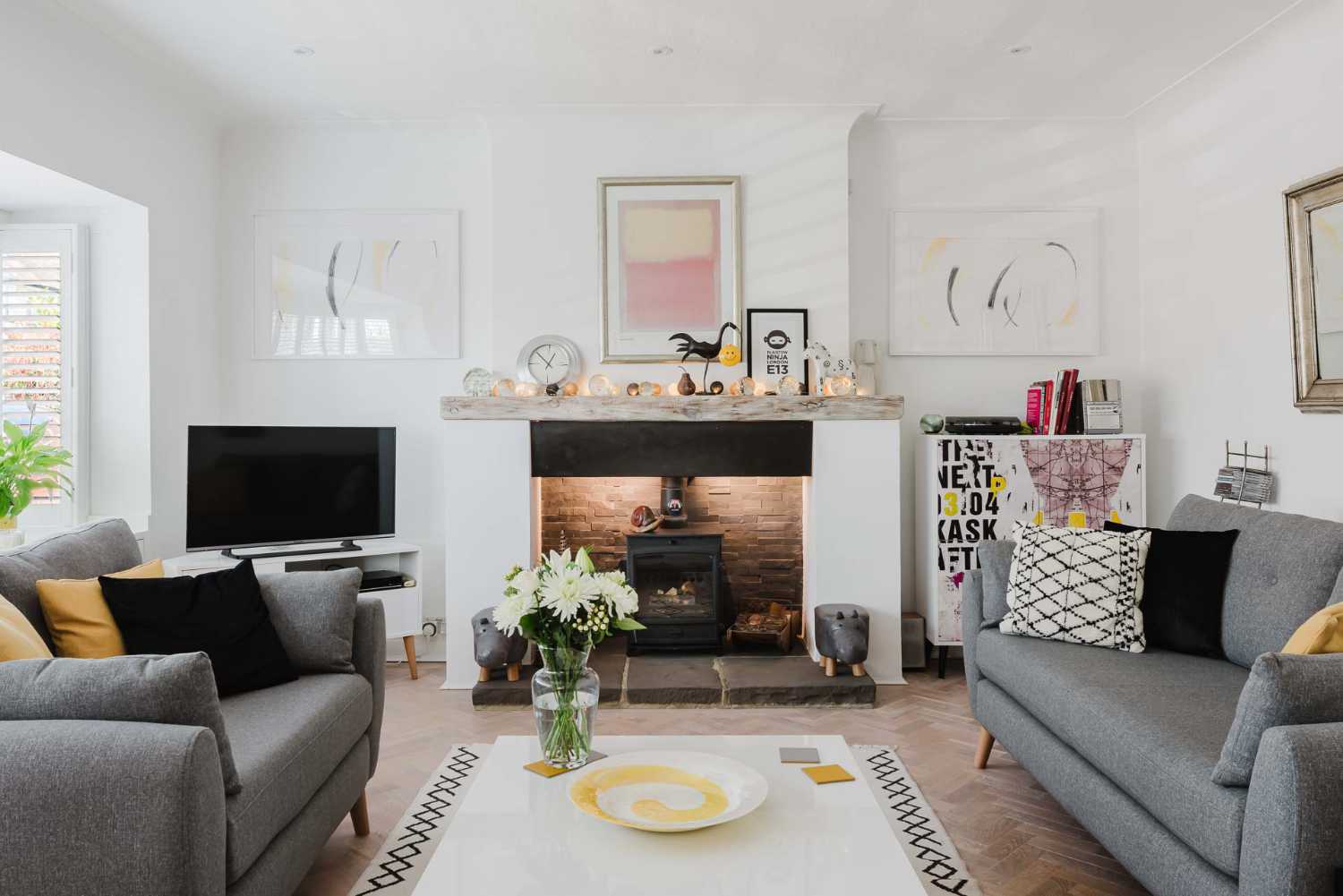 Bright contemporary living room featuring a log burner fireplace, grey sofas, and herringbone wood flooring in a luxury London home.