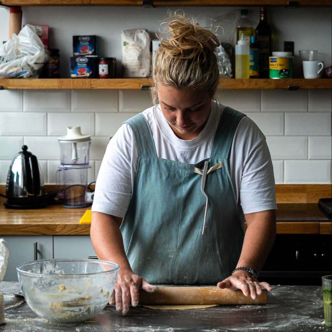 Woman baker rolling dough in a professional kitchen, wearing apron – commercial food photography by Alessandro Pietrosanti
